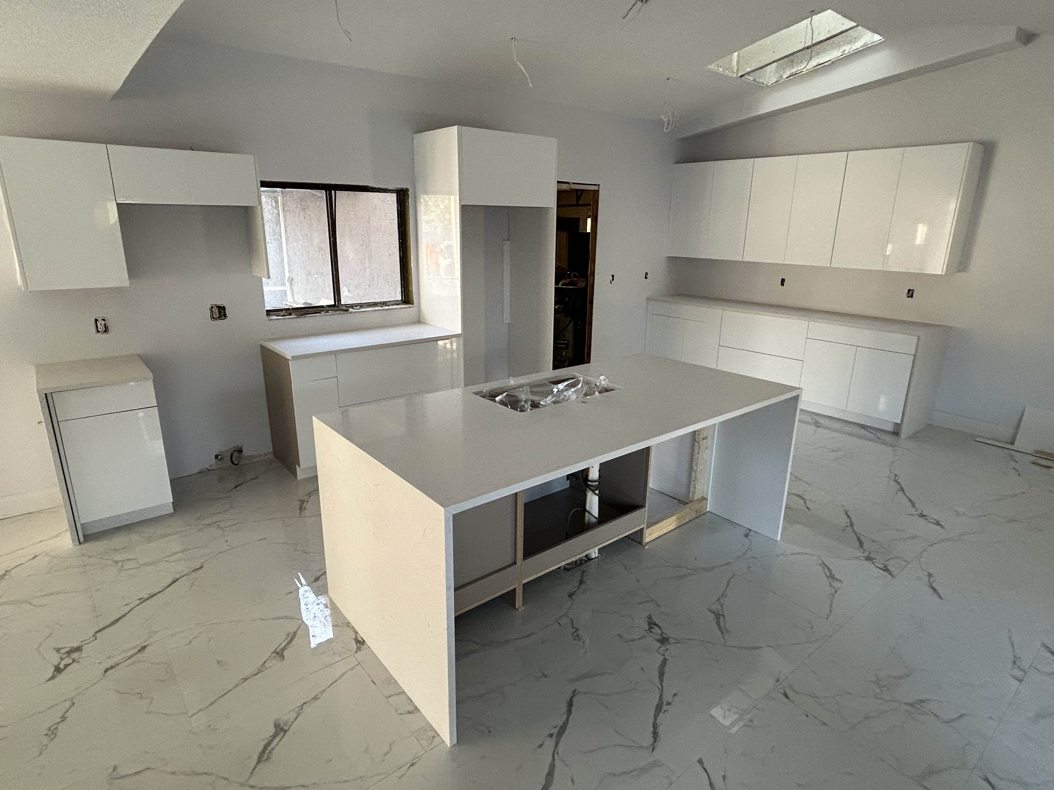 Glossy white kitchen with large island during construction